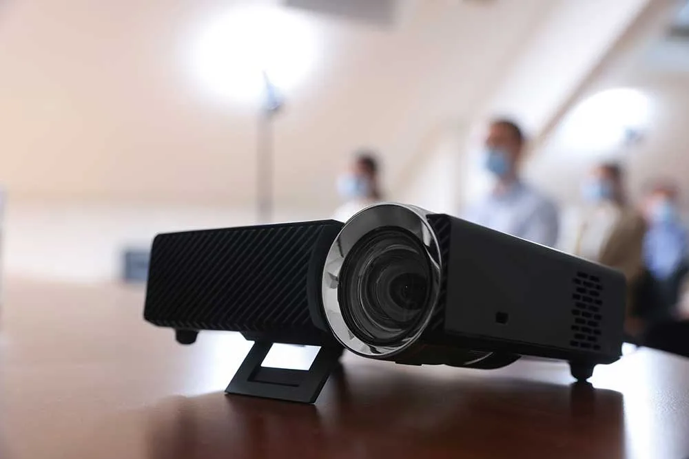projector-sits-on-table-with-blurred-people-in-bac-2026-02-05-18-44-10-utc